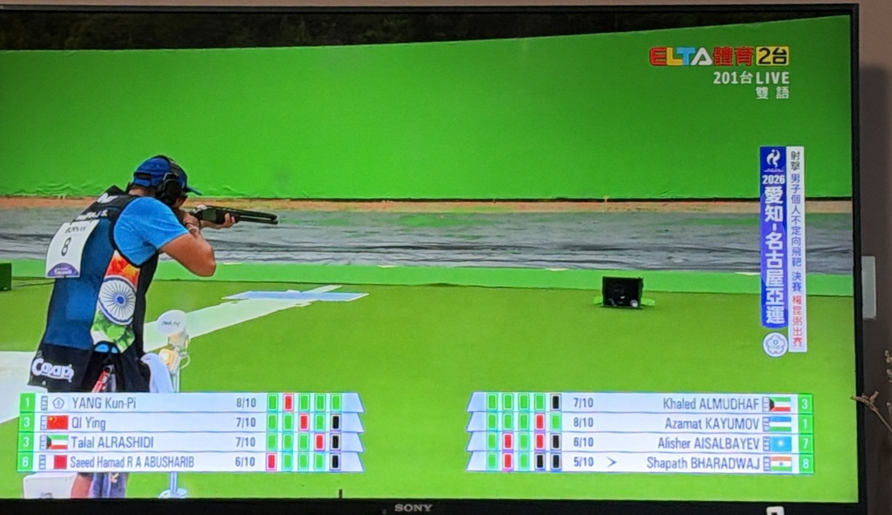 亞運射擊電視轉播中的決賽場景，印度選手 Shapath Bharadwaj 正在瞄準，畫面顯示各選手進度