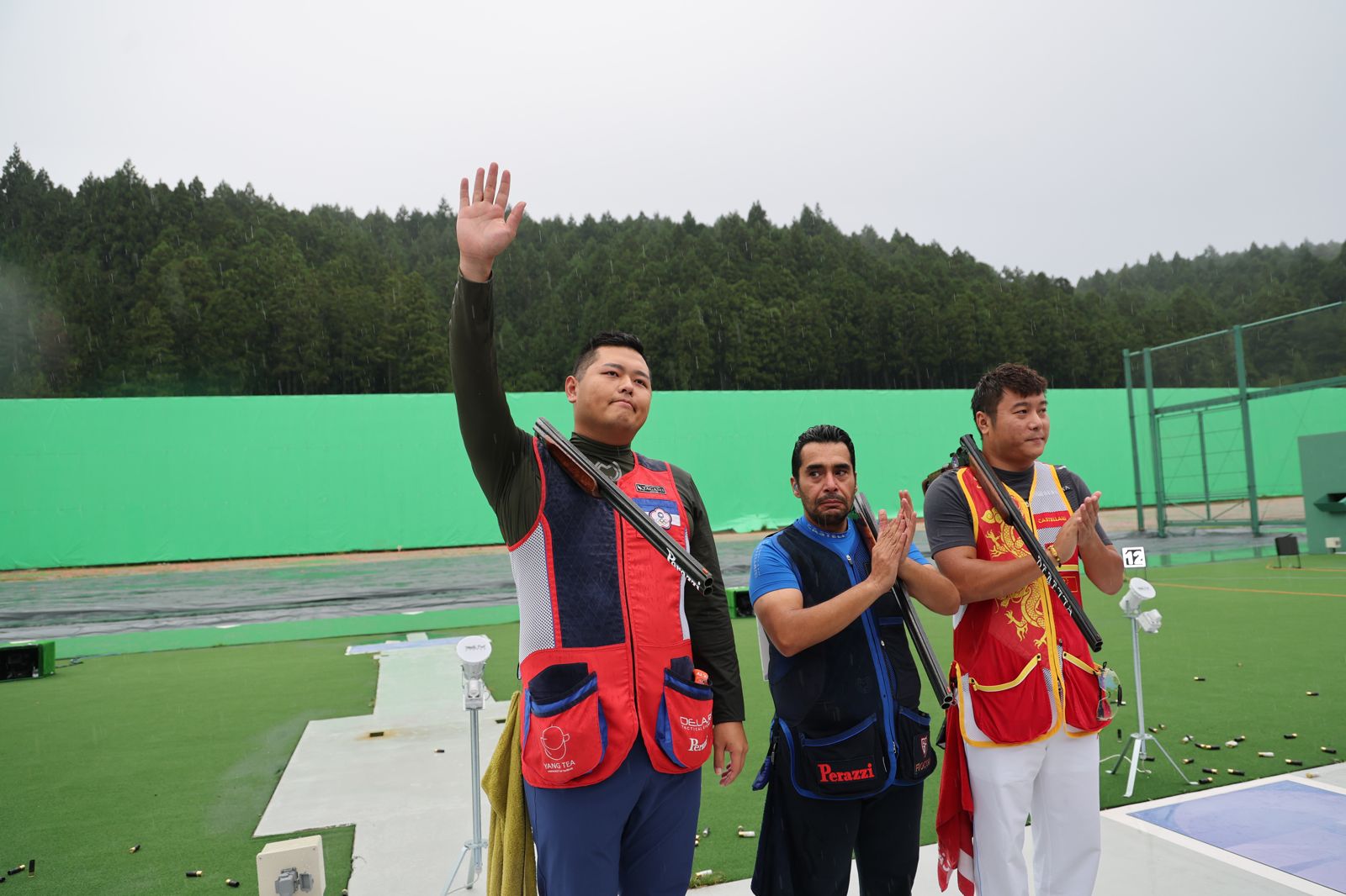 大雨中的亞運射擊場上，楊昆弼舉手致意，科威特選手 Khaled Al-Mudhaf 在一旁鼓掌